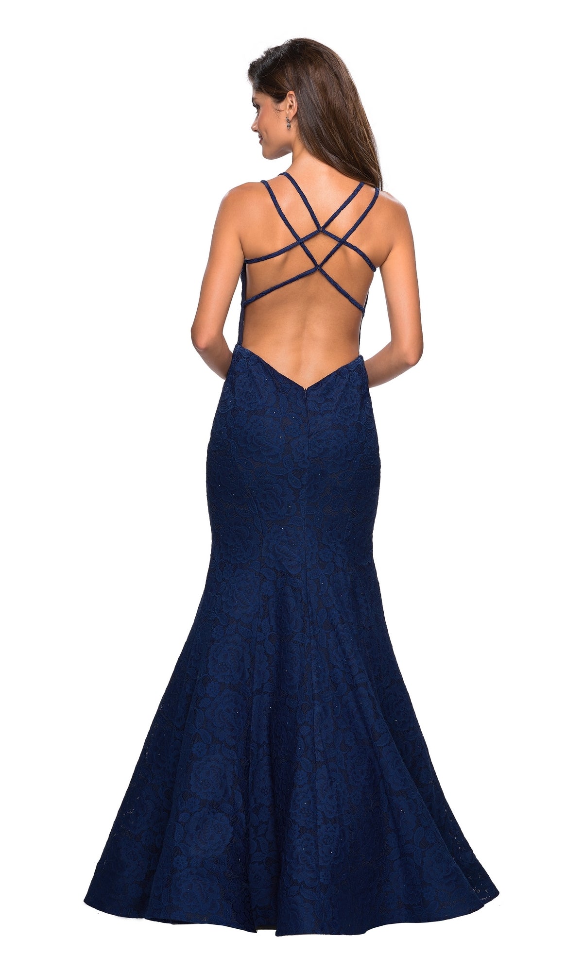 A woman wearing the Backless Lace Mermaid Prom Dress: La Femme 27560—a navy blue, floor-length, fitted gown with a flared hem and crisscrossed open-back straps—looks stunning and ready to make an entrance at prom.